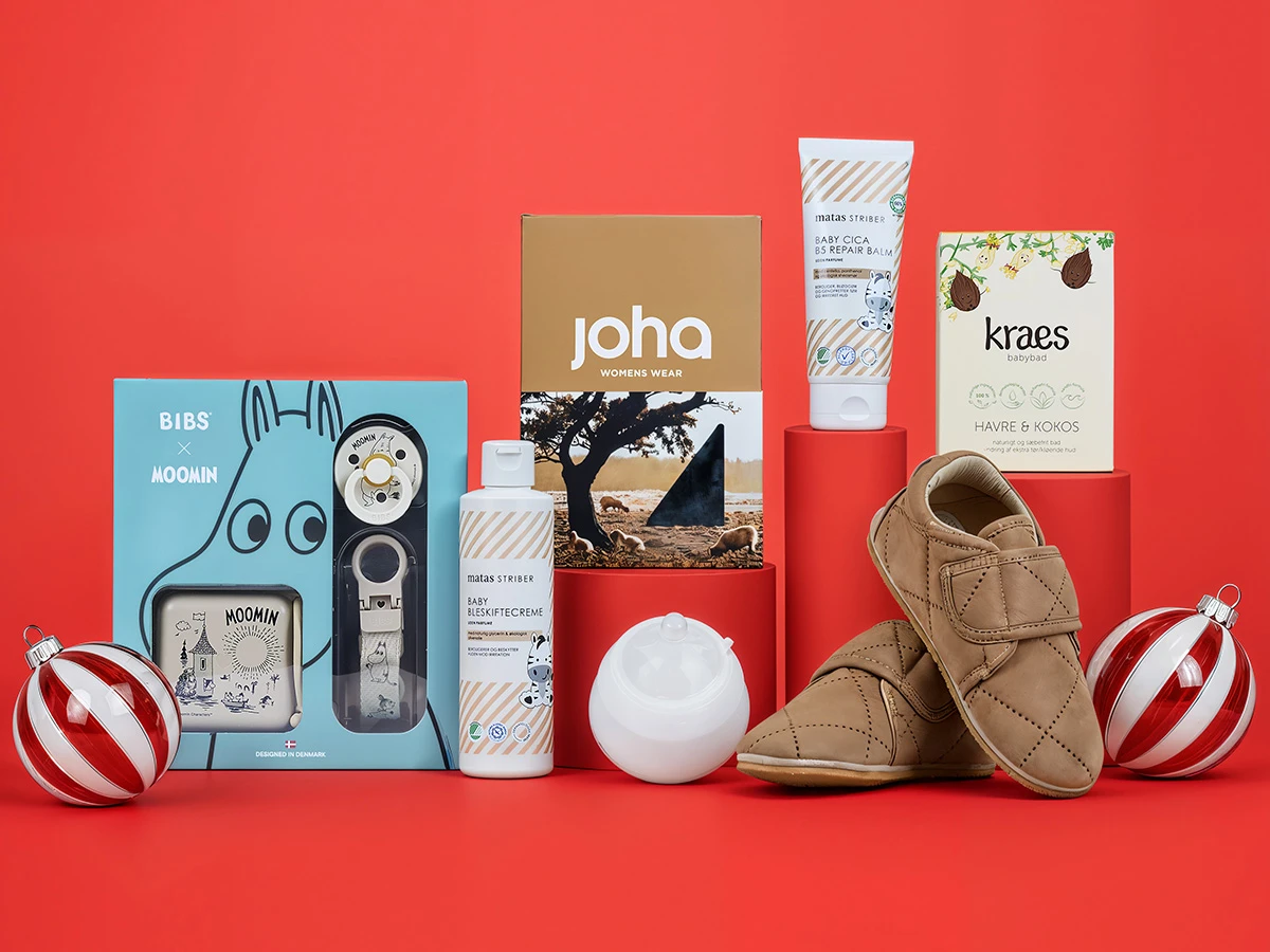 En festlig udstilling af babyprodukter: sutter, hudpleje, babybad, brune sko og en æske Joha tøj.