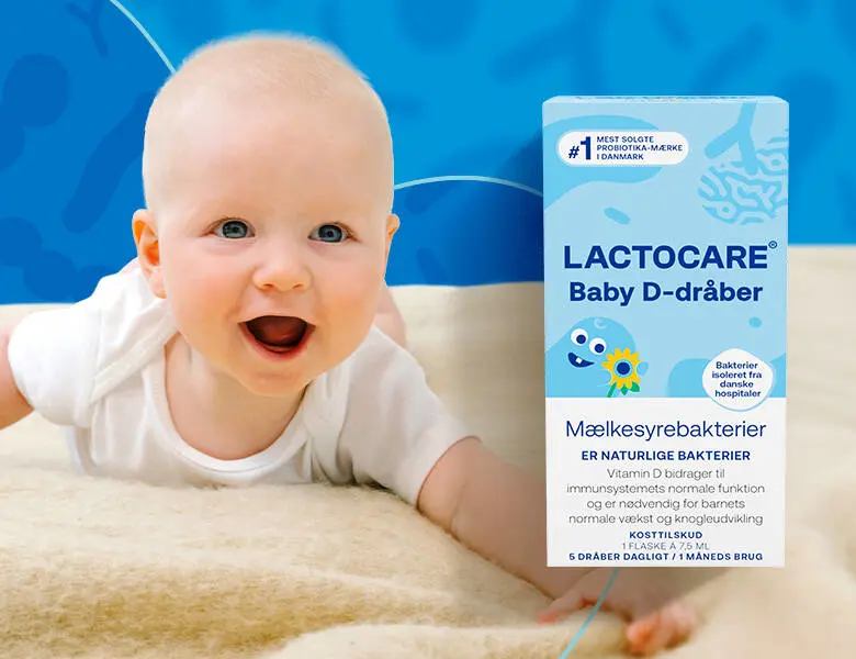 Baby på lyst uldtæppe med blå baggrund. Der ses Lactocare D-dråber forrest i billedet.