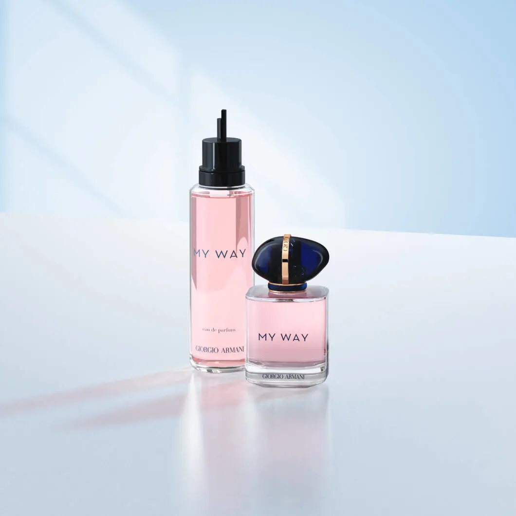 To Giorgio Armani My Way-parfumeprodukter står på en lys overflade foran en blød lyseblå baggrund. Til venstre ses en høj refillflaske med lyserød parfume og sort pumpe. Til højre står den originale My Way-parfumeflaske med mørkeblåt låg og gulddetaljer. Billedet har et elegant og moderne udtryk med fokus på luksusparfume og refill-løsninger.