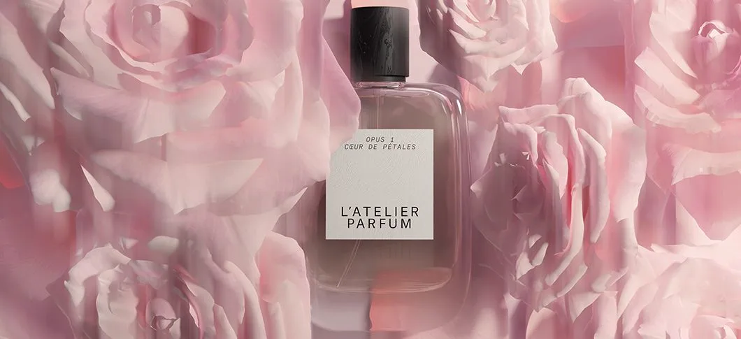Her ses en L'Atelier Parfum flakon foran en baggrund af lyserøde roser.