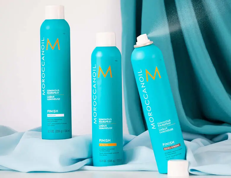 Her ses tre MoroccanOil i deres ikoniske turkise farve. Baggrunden har samme farve samt hvid. 