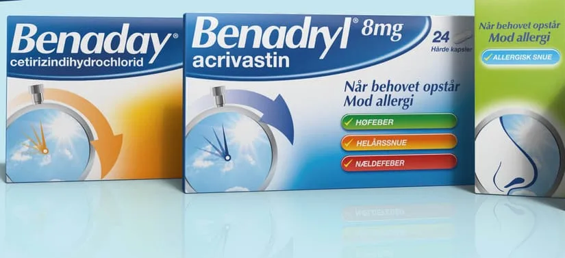 To pakker allergimedicin fra Benadryl står ved siden af hinanden på en lys blå baggrund. Til venstre ses en pakke med teksten “Benaday cetirizindihydrochlorid” i blå og orange farver med et grafisk ur-ikon. Til højre ses en større pakke med teksten “Benadryl 8 mg acrivastin”, også med et ur-ikon og en blå pil. På den højre pakke står teksten “Når behovet opstår – mod allergi” samt tre farvede markeringer med ordene “Høfeber”, “Helårssnue” og “Nældefeber”. Yderst til højre anes en tredje pakke i grønne nuancer med en illustration af en næse. Udtrykket er informativt og medicinsk med klare farvekoder.