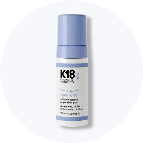 Her ses et billede af et hårplejeprodukt fra K18 placeret centralt mod en lys, rund baggrund. På produktet står teksten “K18 BIOMIMETIC HAIRSCIENCE leave-in molecular repair hair mask”. Flasken er i hvid emballage med pumpefunktion.