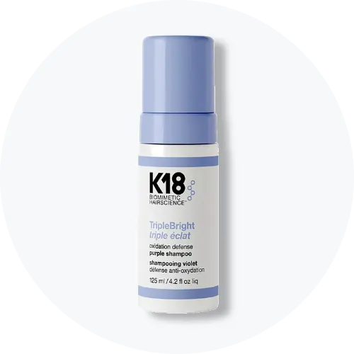 Her ses et billede af et hårplejeprodukt fra K18 placeret centralt mod en lys, rund baggrund. På produktet står teksten “K18 BIOMIMETIC HAIRSCIENCE leave-in molecular repair hair mask”. Flasken er i hvid emballage med pumpefunktion.