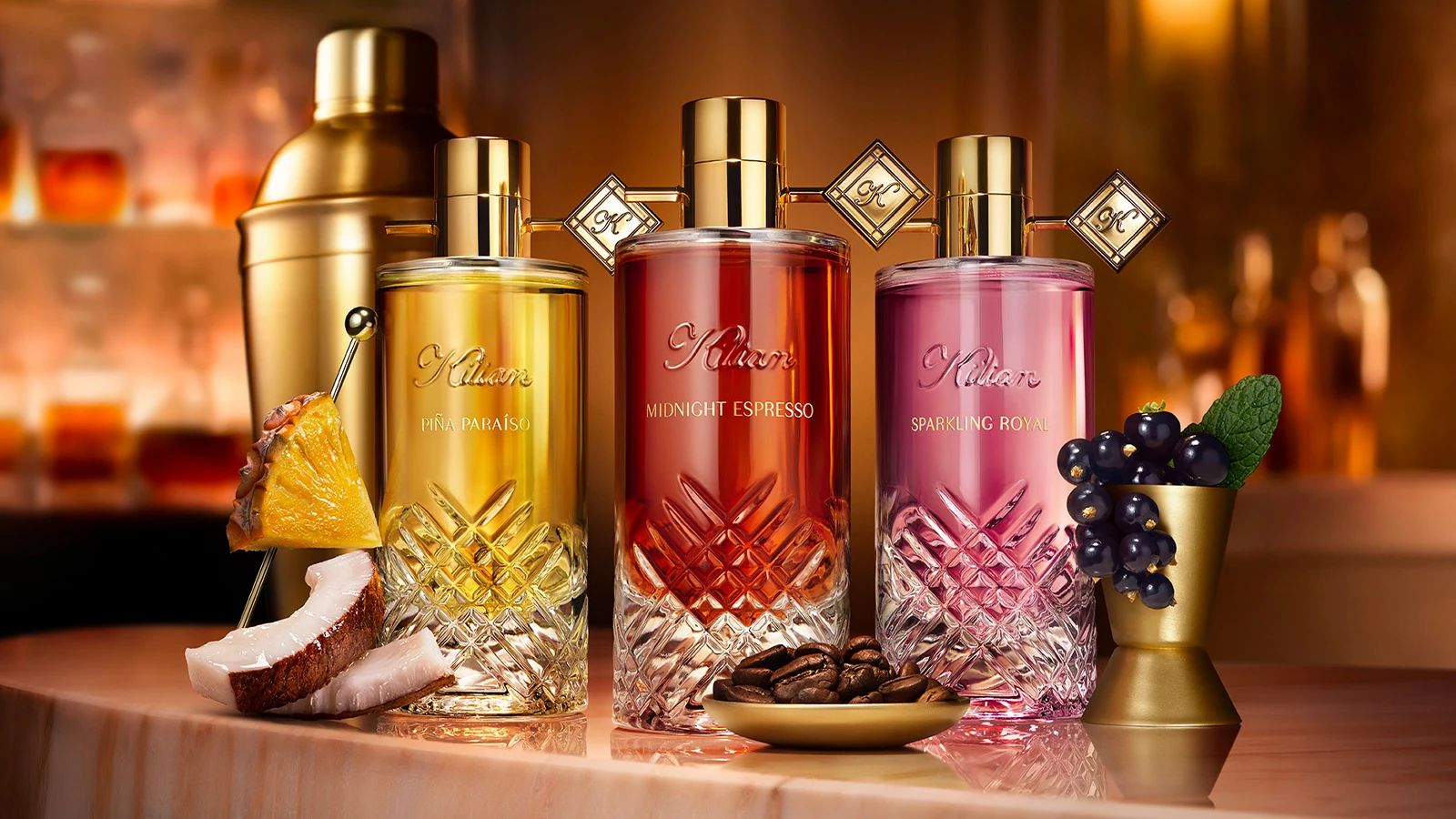 Kilian parfumer: Piña Paraíso (gul), Midnight Espresso (rød), Sparkling Royal (pink). Står på bar med kaffebønner, ananas, kokos, solbær.