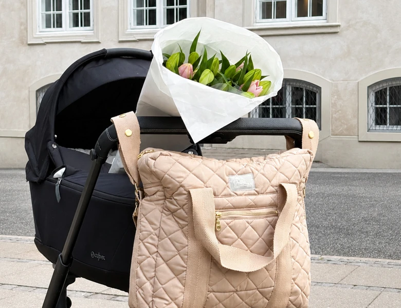 Quiltet pusletaske hænger på en barnevogn med en buket tulipaner i kalechen på en gade i byen