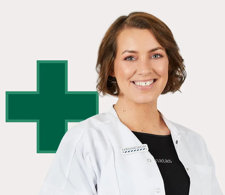 En smilende person med kort brunt hår står foran en lys baggrund iført hvid kittel med navneskilt og sort trøje med Matas-logo. Ved siden af personen ses et stort grønt kors, som forbindes med apotek eller sundhedsfaglig rådgivning.