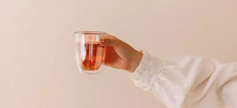 Her ses en lyserød baggrund med en arm, som har en skjorte på. I hånden holdes en kop te.