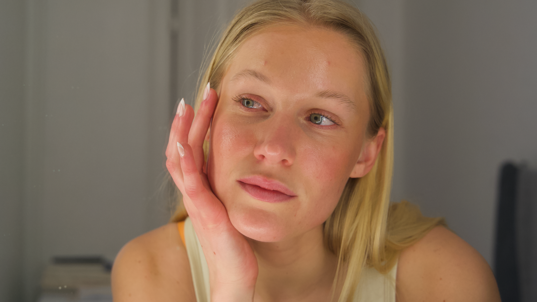 En ung person med blondt hår, der ser eftertænksom ud, med en hånd hvilende på kinden.