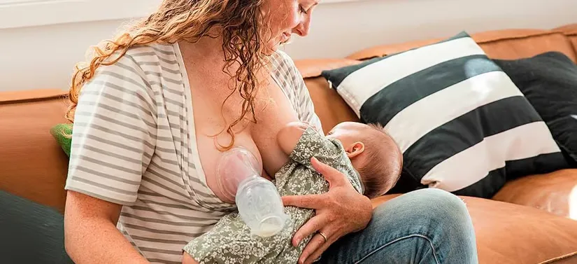Her ses en kvinde som ammer på det ene bryst og har en brystpumpe på det andet. Hun sidder i en brun sofa.