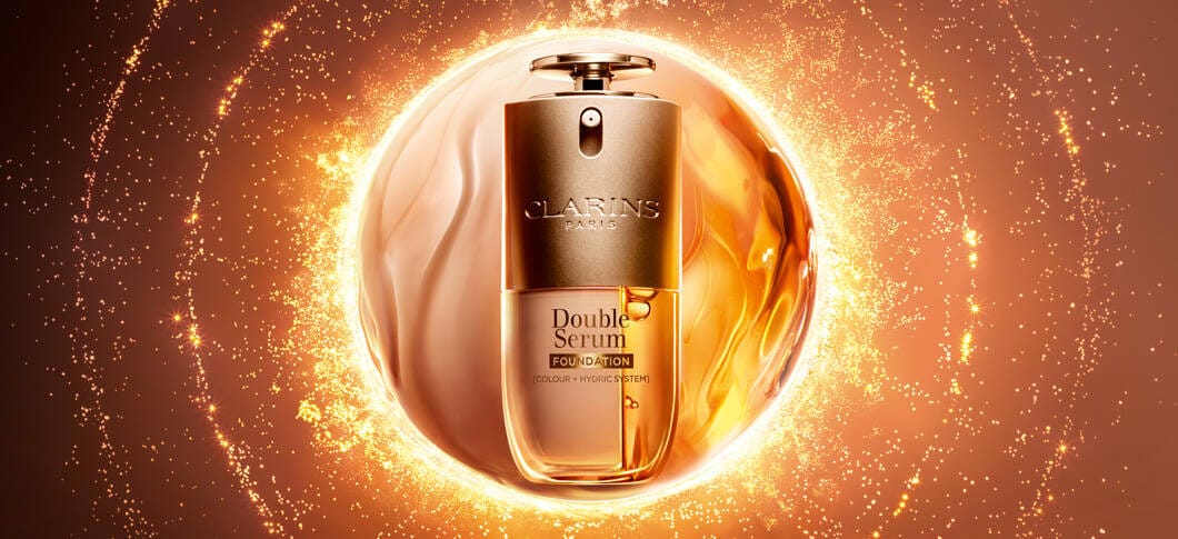 Her ses en Clarins Double Serum Foundaiton foran en cirkel, der ligner halvt fouundation og halvt serum. Baggrunden er gylden orange.