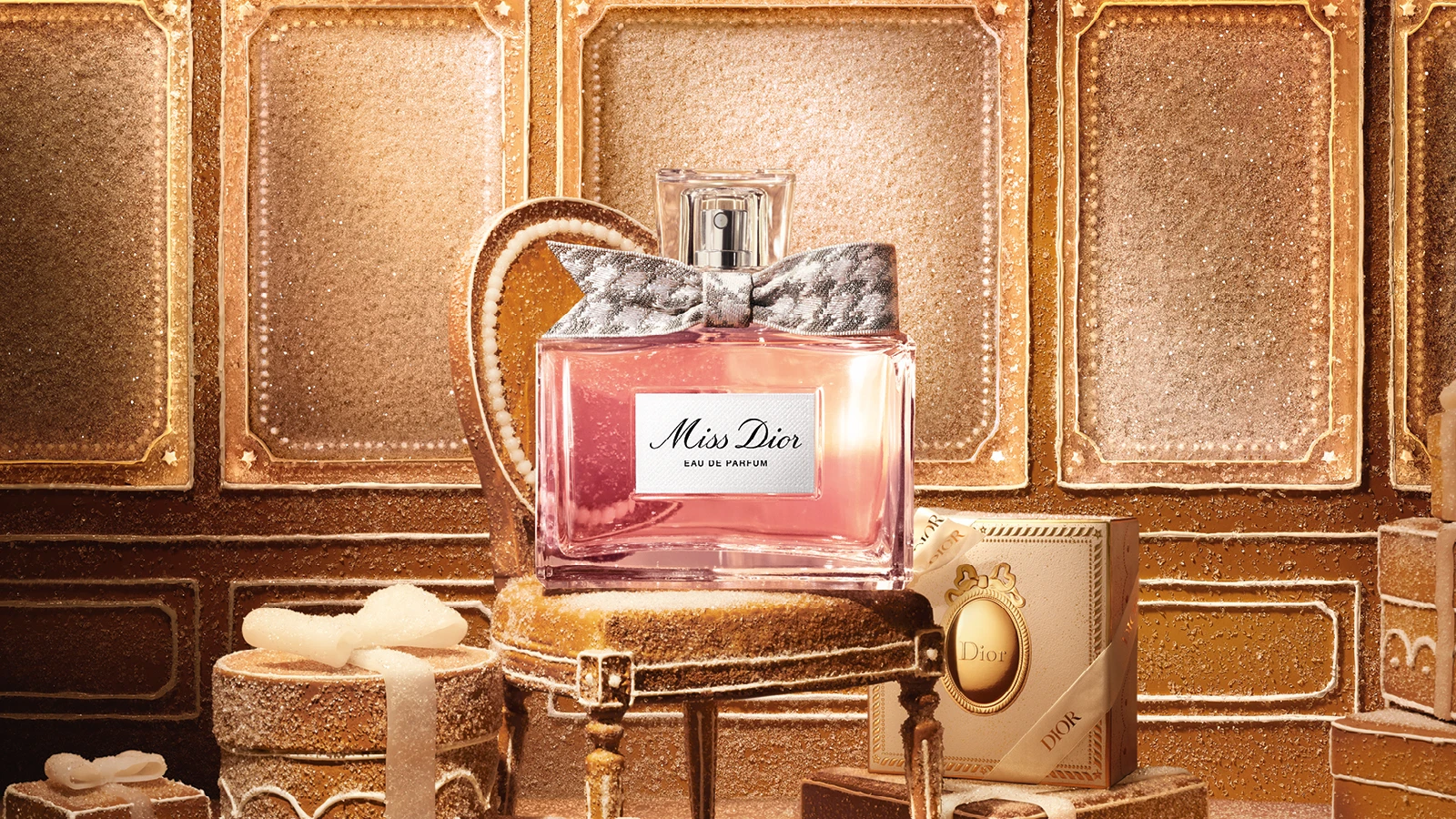 Miss Dior Eau de Parfum flaske med sølvsløjfe på sukkerdækket stand. Baggrund af glitrende honningkagevæg og Dior-gaveæsker.