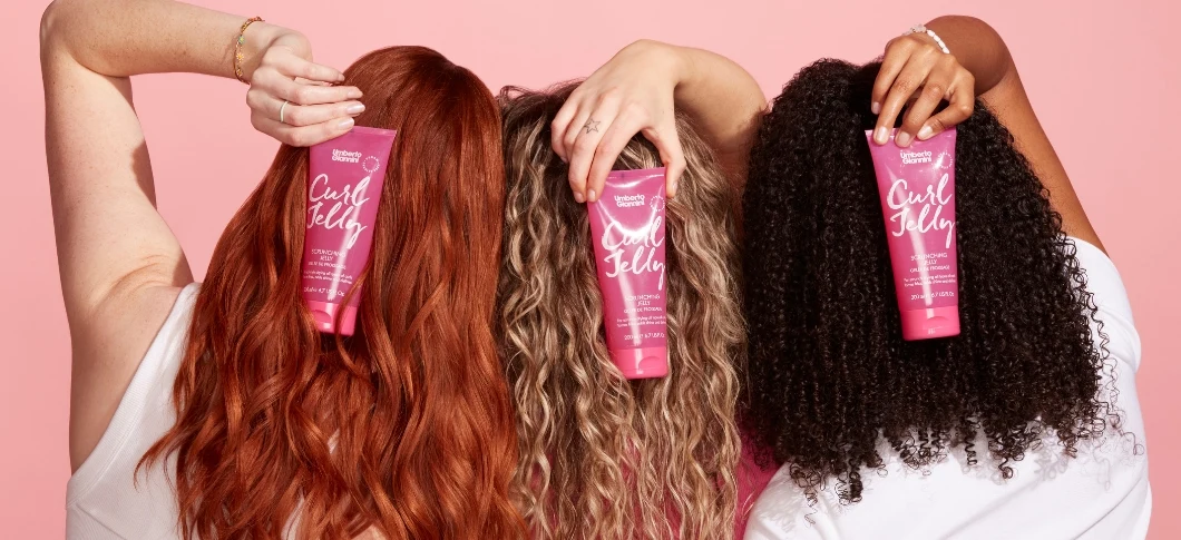 Tre personer med varierende krøllede hårtyper holder lyserøde tuber af Umberto Giannini Curl Jelly.