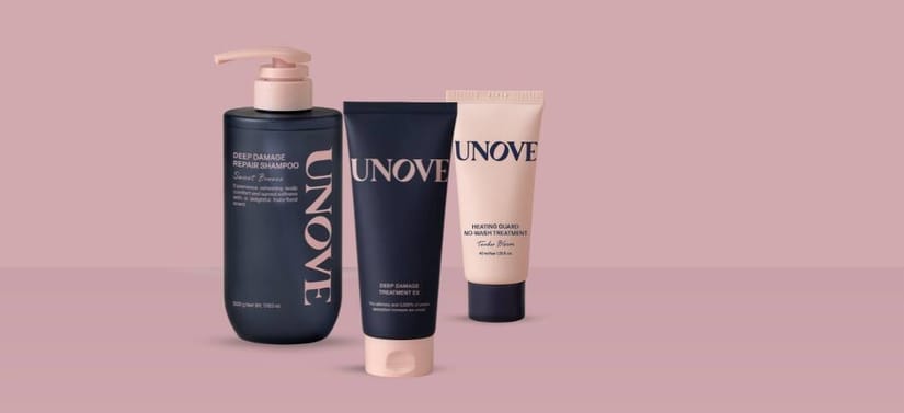 Her ses et billede med tre hårplejeprodukter fra UNOVE placeret mod en lyserød baggrund. På produkterne står blandt andet “DEEP DAMAGE REPAIR SHAMPOO”, “DEEP DAMAGE TREATMENT EX” og “NO-WASH TREATMENT”. Produkterne er i mørkeblå og beige emballage.
