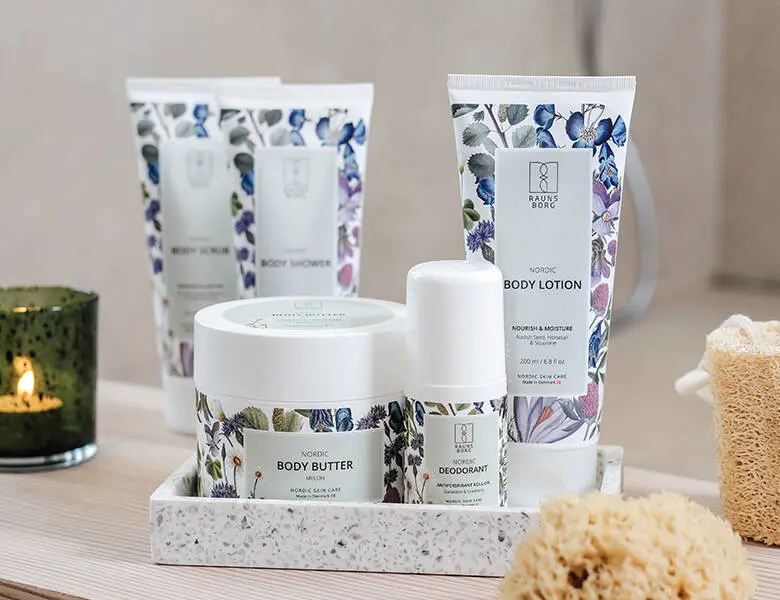 Her ses hvide stående produkter med blomster på. Nogle står i en stenbakke og andre står på den lyse træoverflade.
