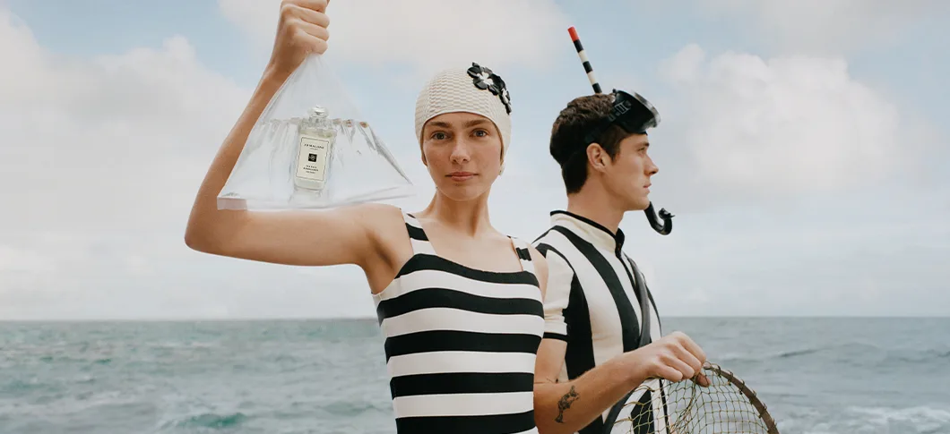 Her ses to personer i noget, der ligner en ørken. Sammen holder de en meget stor Jo Malone parfume.