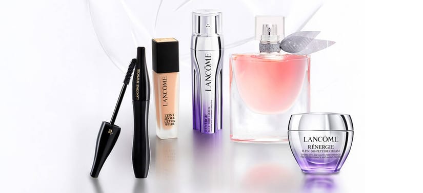 Her ses et billede med flere produkter fra Lancôme placeret på en lys, reflekterende overflade mod en lys baggrund. Produkterne inkluderer en mascara, en foundation med teksten “TEINT IDOLE ULTRA WEAR”, en serumflaske med teksten “LANCÔME”, en parfumeflakon med lyserød væske og en cremekrukke med teksten “RÉNERGIE H.P.N. 300-PEPTIDE CREAM”.