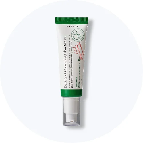 Her ses et AXIS-Y Dark Spot Correcting Glow Serum i hvid og grøn emballage på en lys baggrund.