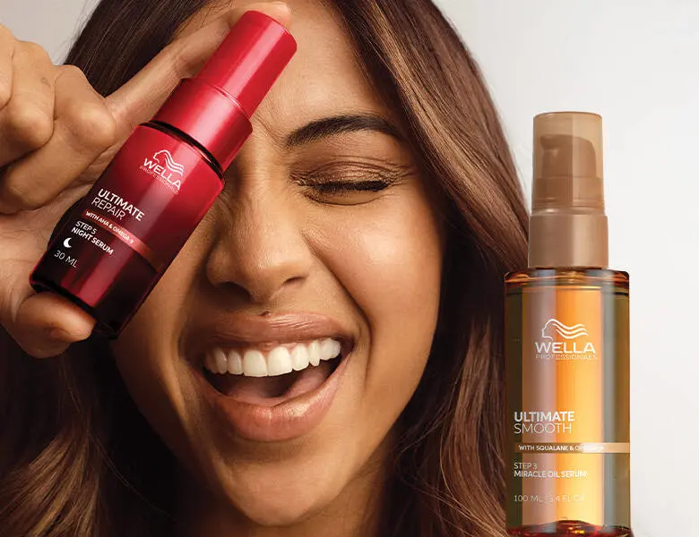 Her ses et billede af en person, der smiler og holder et hårserum fra Wella Professionals op foran ansigtet. Ved siden af ses endnu et produkt fra Wella Professionals med teksten “ULTIMATE SMOOTH”. Produkterne er i røde og gyldne nuancer.