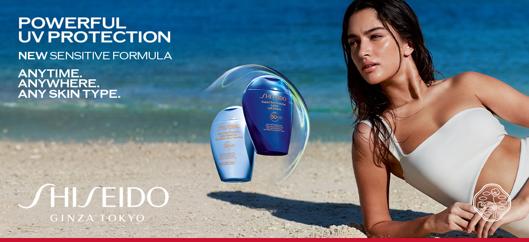 Her ses et billede med solplejeprodukter fra Shiseido placeret på en strand ved havet. På billedet står teksten “POWERFUL UV PROTECTION”, “NEW SENSITIVE FORMULA” samt “ANYTIME. ANYWHERE. ANY SKIN TYPE.” Til højre ses en person i hvid badetop, og nederst står teksten “SHISEIDO GINZA TOKYO”.