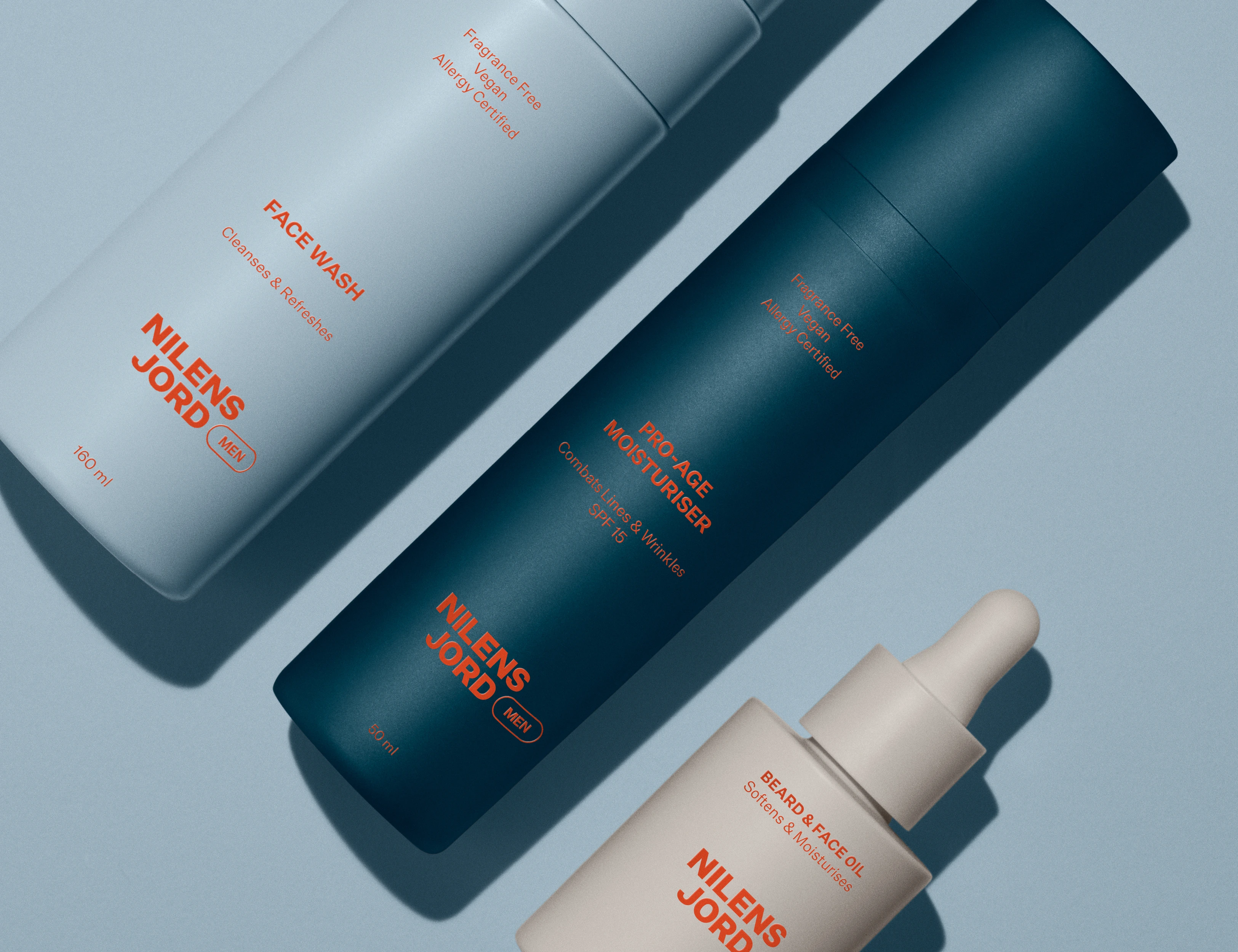 Her ses et billede med hudplejeprodukter fra Nilens Jord Men placeret mod en blå baggrund. På produkterne står blandt andet “FACE WASH”, “PRO-AGE MOISTURISER” og “BEARD & FACE OIL”. Produkterne er i hvide og mørkeblå nuancer.