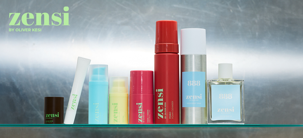 Her ses et billede med flere produkter fra zensi placeret på en glashylde mod en metallisk baggrund. På billedet står teksten “zensi BY OLIVER KESI”, og på produkterne ses blandt andet “zensi” og “888”. Produkterne er i forskellige farver som grøn, blå, gul, rød og sølv.