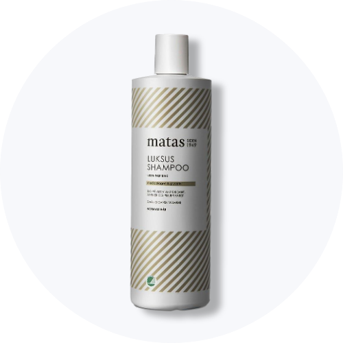 Her ses et billede af en shampoo fra Matas placeret centralt mod en lys baggrund. Flasken er i hvid med stribede detaljer, og på den står teksten “Luksus shampoo”.