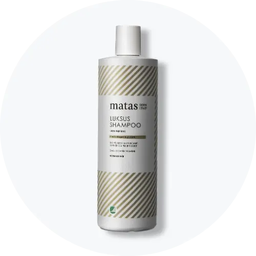 Her ses et billede af en shampoo fra Matas placeret centralt mod en lys baggrund. Flasken er i hvid med stribede detaljer, og på den står teksten “Luksus shampoo”.