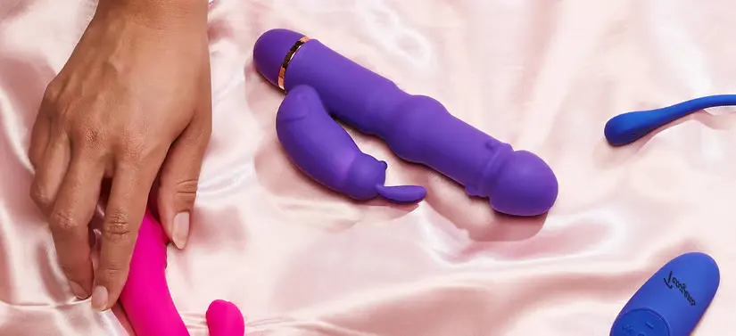 Her ses et lyserødt silkelagen med forskellige produkter i blå og pink. En hånd tager det i pink.
