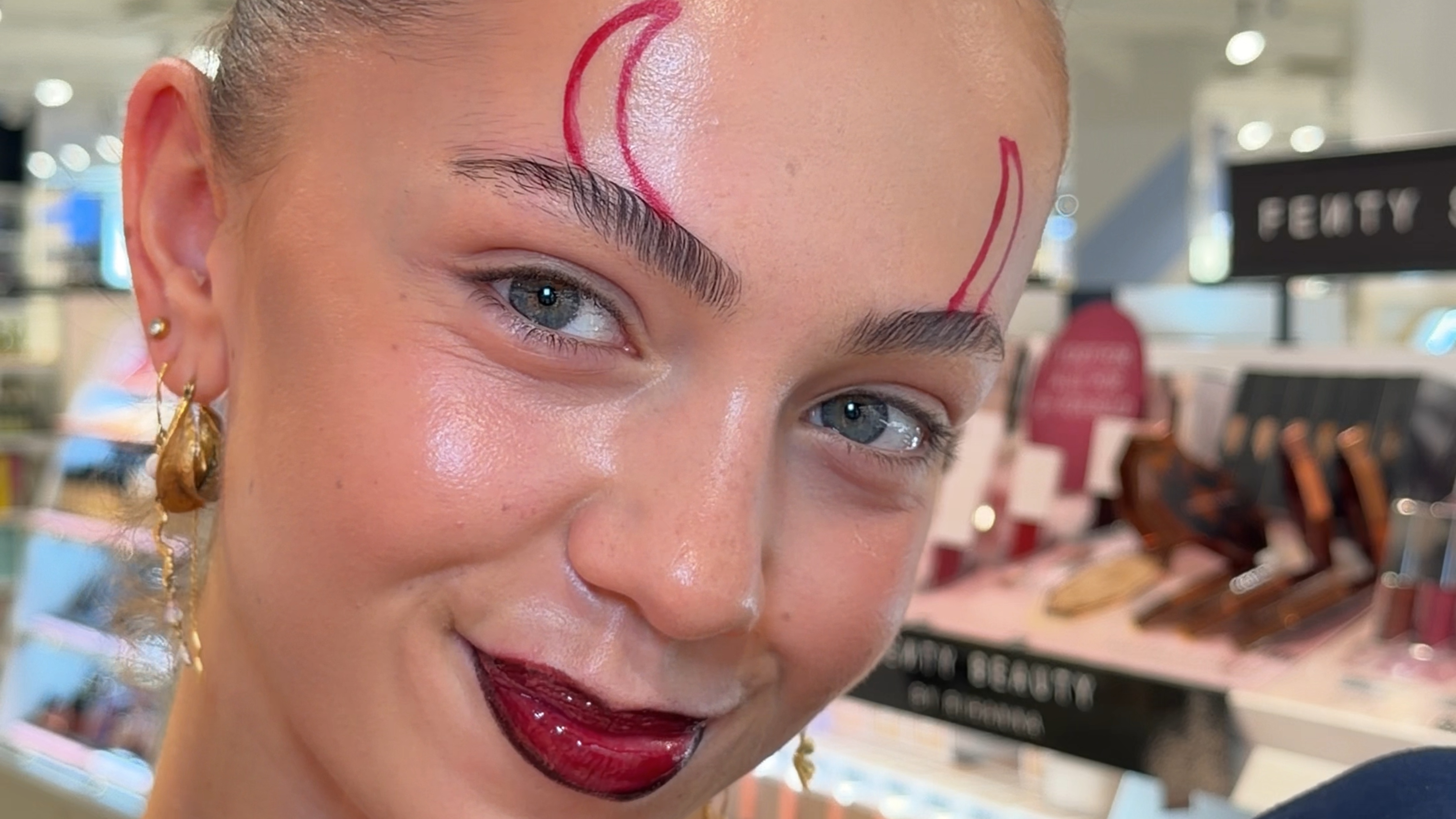 Her ses en person med mørkt hår og makeup med røde læber og øjenmakeup. På kinden ses røde streger og små prikker som en del af et Halloweenlook.