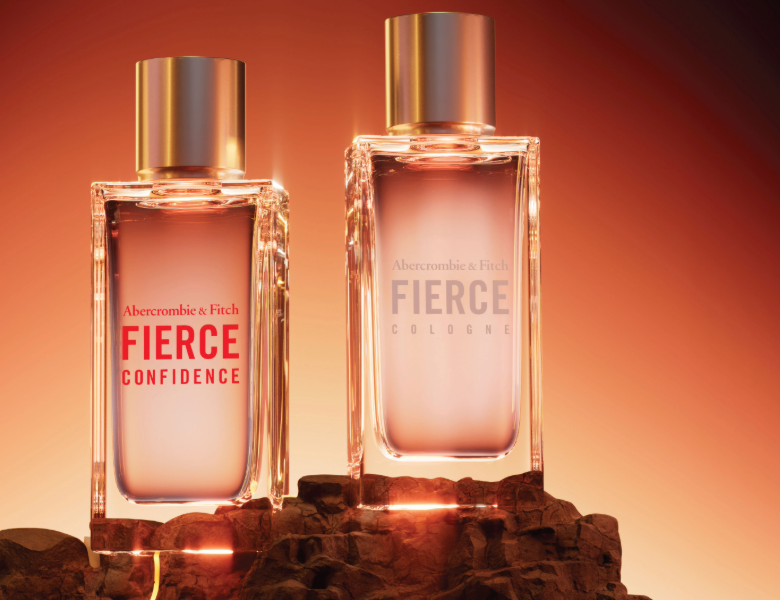 Her ses et billede med to parfumeflakoner fra Abercrombie & Fitch placeret på en klippeagtig overflade mod en varm orange baggrund. På flakonerne står blandt andet teksterne “FIERCE CONFIDENCE” og “FIERCE COLOGNE”. Flakonerne har guldfarvede låg og transparente glasflasker i varme nuancer.