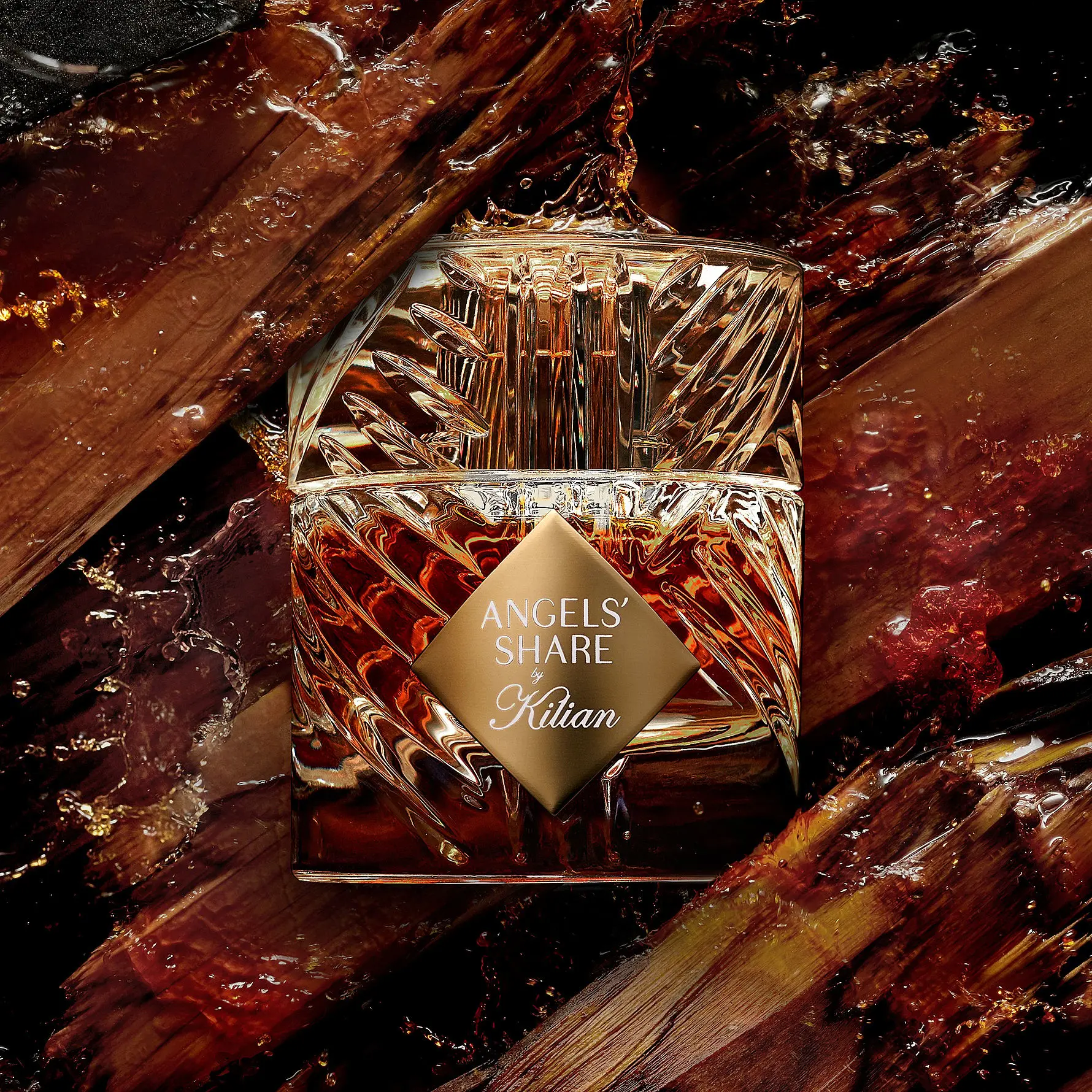Her ses et billede af en parfumeflakon fra Kilian placeret centralt mod en mørk baggrund. På flakonen står teksten “OLD FASHIONED by Kilian”. Flakonen har et facetteret design i klare og gyldne nuancer og er omgivet af træstykker og små partikler.