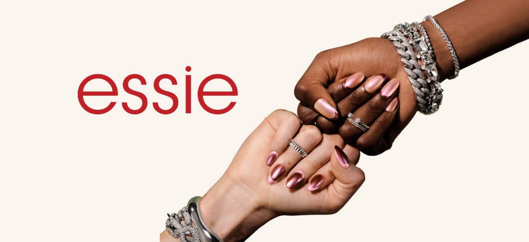 Her ses en beige baggrund og "essie" skrevet med rød. Der ses to hænder holdt mod hinanden så man kan se deres neglelak på.