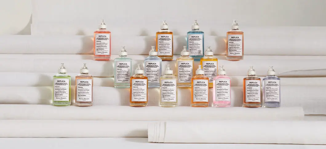 Her ses flere Maison Margiela Replica-parfumer opstillet i rækker på forskellige trin og med en lys baggrund.