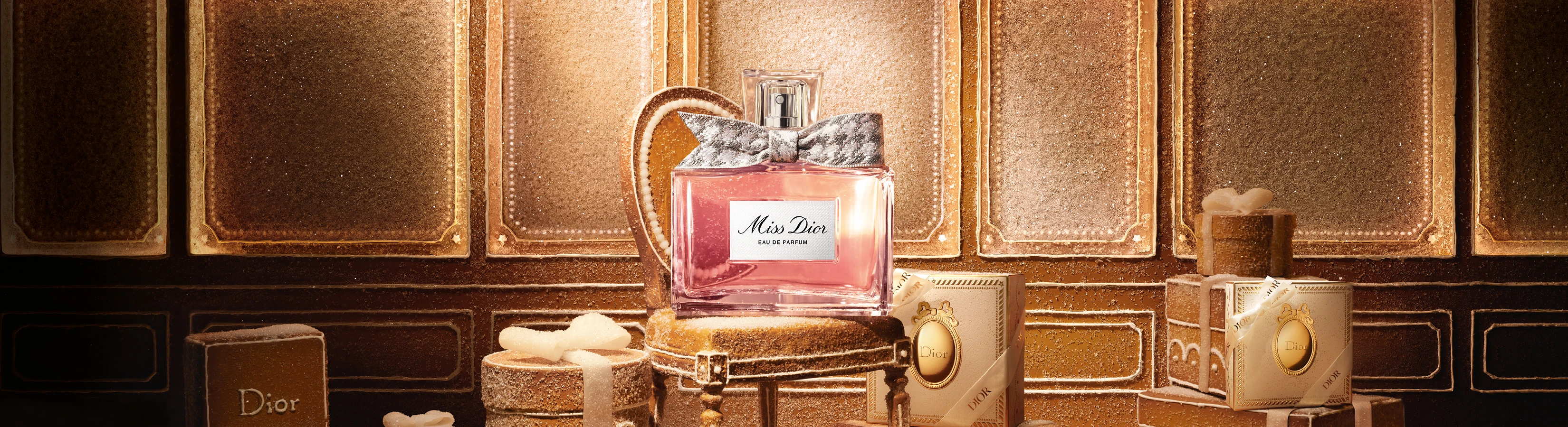 Miss Dior Eau de Parfum flaske med lyserød væske og sølvsløjfe, på sukkerede, gyldne gaveæsker med festlig baggrund.