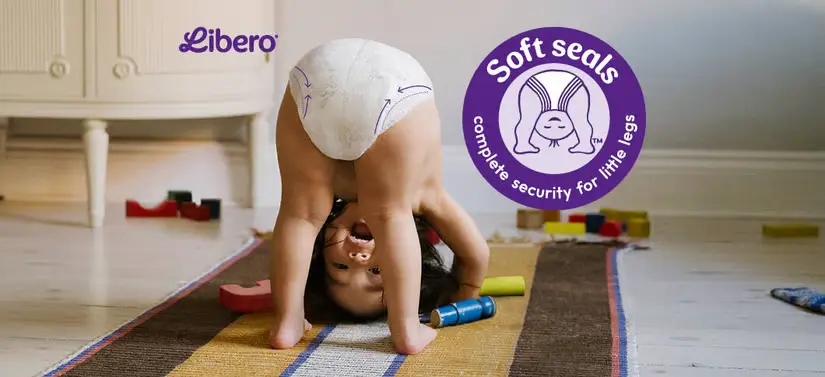Her ses en baby som vender hovedet nedad. Baggrunden er en stue med noget legetøj og gulvtæppe. Der ses desuden to Lilla logoer.