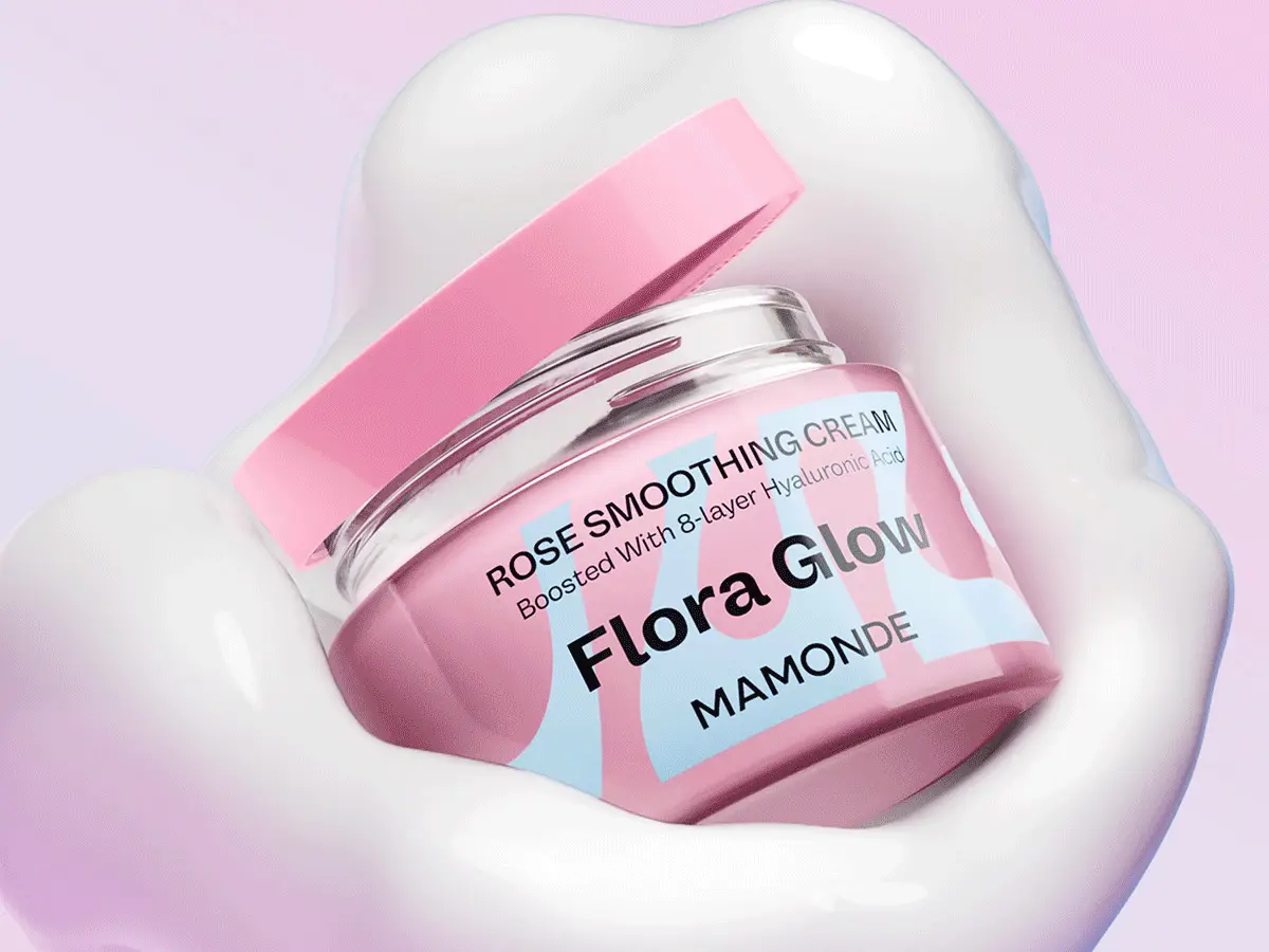 Her ses et billede af en lyserød ansigtscreme fra Mamonde placeret på en hvid, cremet baggrund mod en lyserød baggrund. På emballagen står blandt andet “Flora Glow”, “Rose Smoothing Cream” og “Boosted With 8-layer Hyaluronic Acid”. Krukken har et lyserødt låg, der er placeret let på klem.
