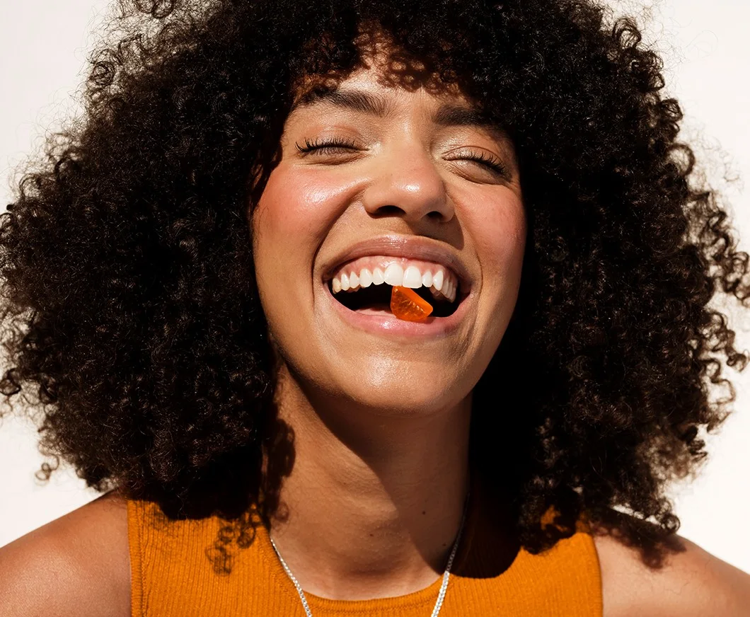 Her ses en glad kvinde med orange top på. I munden har hun en orange c-vitamin vingummi. Under hende står der "C-vitamin".