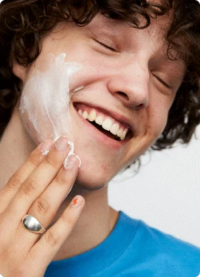 Her ses en ung dreng, som tager creme i ansigtet.