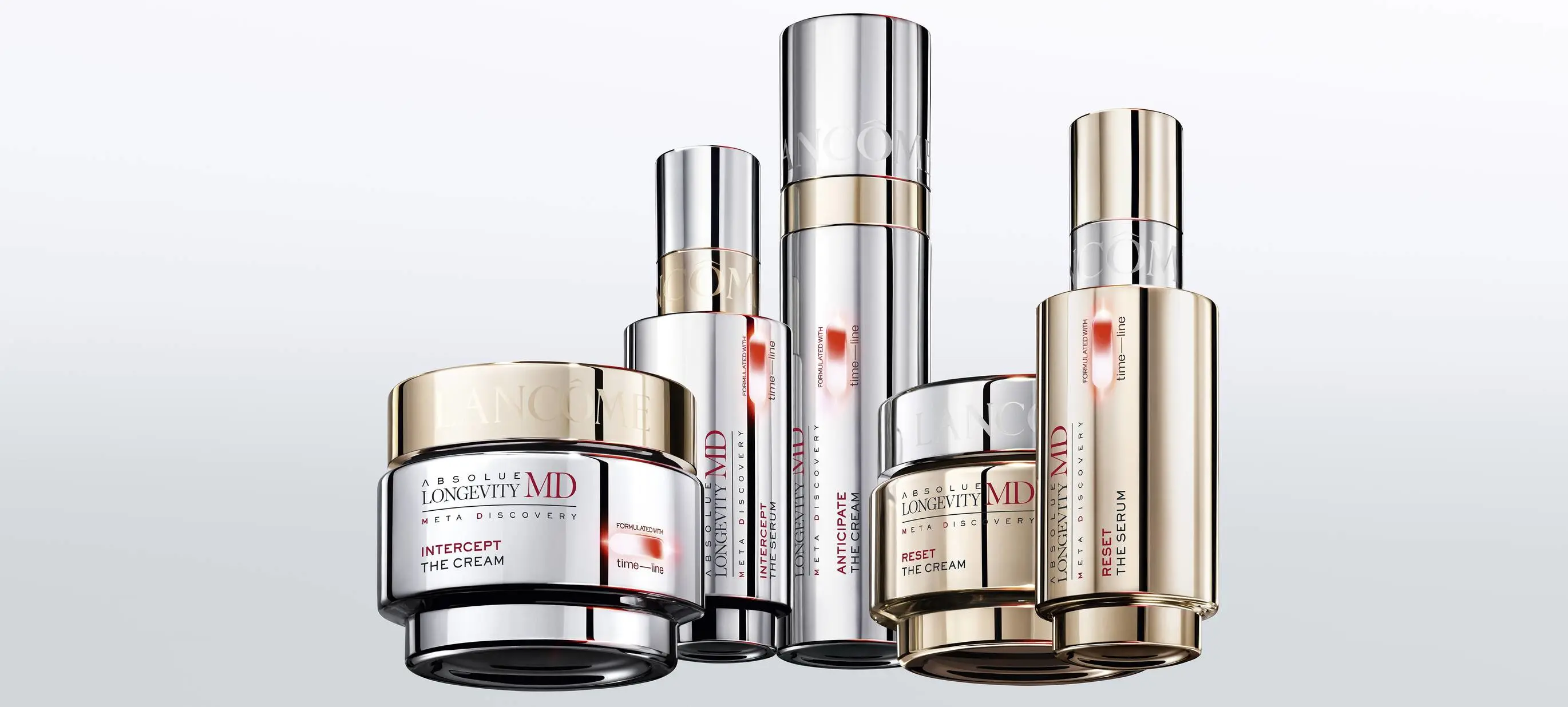 Reklamebillede af flere luksuriøse hudplejeprodukter fra Lancômes serie “Absolue Longevity MD – Meta Discovery” arrangeret på række mod en lys grå baggrund. Produkterne består af to cremekrukker og tre høje serumflasker i blanke sølv- og guldfarvede emballager med røde detaljer. På produkterne står blandt andet “Intercept The Cream”, “Anticipate The Cream”, “Intercept The Serum”, “Reset The Cream” og “Reset The Serum”. Produkterne varierer i størrelse og form, men har alle et eksklusivt og futuristisk design med metalliske overflader. Billedet har et elegant og minimalistisk udtryk med fokus på luksus, avanceret hudpleje og anti-age produkter.