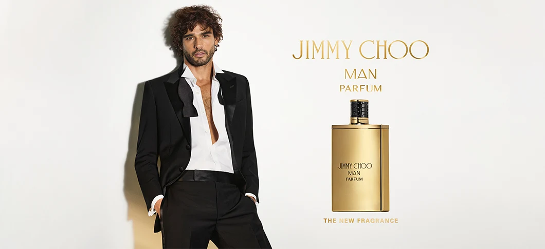 Her ses et billede af en person iført et sort jakkesæt og en hvid skjorte mod en lys baggrund. Til højre ses en gylden parfumeflakon med teksten “Jimmy Choo Man Parfum”. Øverst står teksten “JIMMY CHOO MAN PARFUM”, og nederst står “THE NEW FRAGRANCE”.