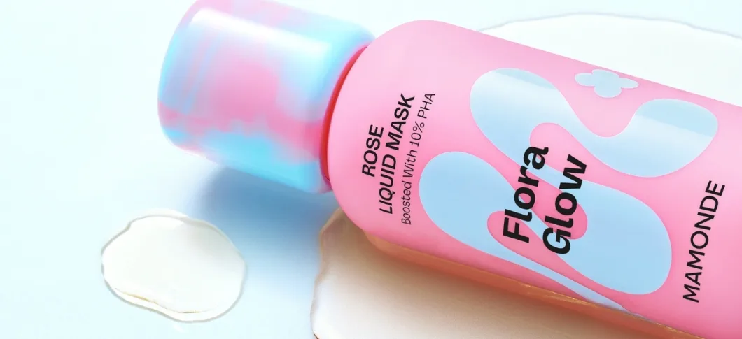 Her ses en Mamonde Rose Liquid Mask i pink og lyseblå emballage på en lys baggrund med væske omkring produktet.
