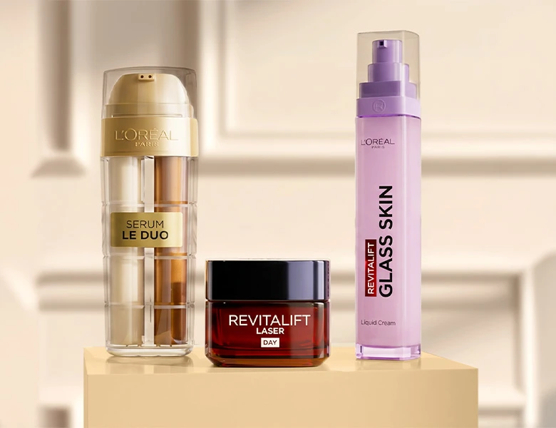 Her ses tre L’Oréal Paris hudplejeprodukter på en beige sokkel: Serum Le Duo, Revitalift Laser Day Cream og Revitalift Glass Skin Liquid Cream.
