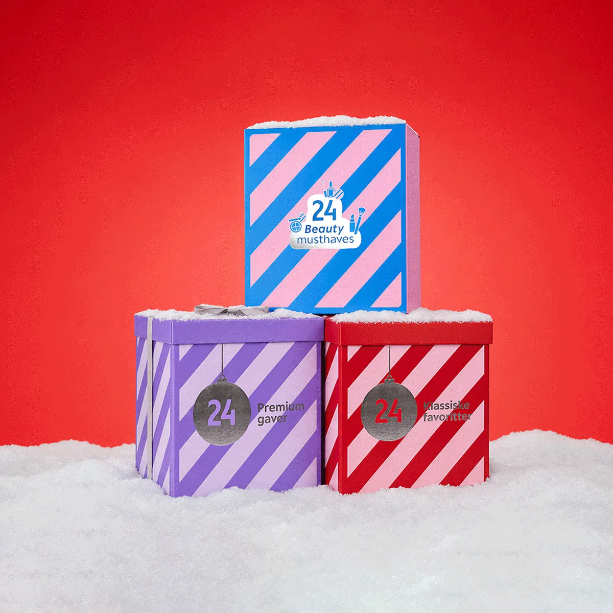 Tre farverige adventskalendere på sne: Blå '24 Beauty musthaves', lilla '24 Premium gaver', rød '24 Klassiske favoritter'.