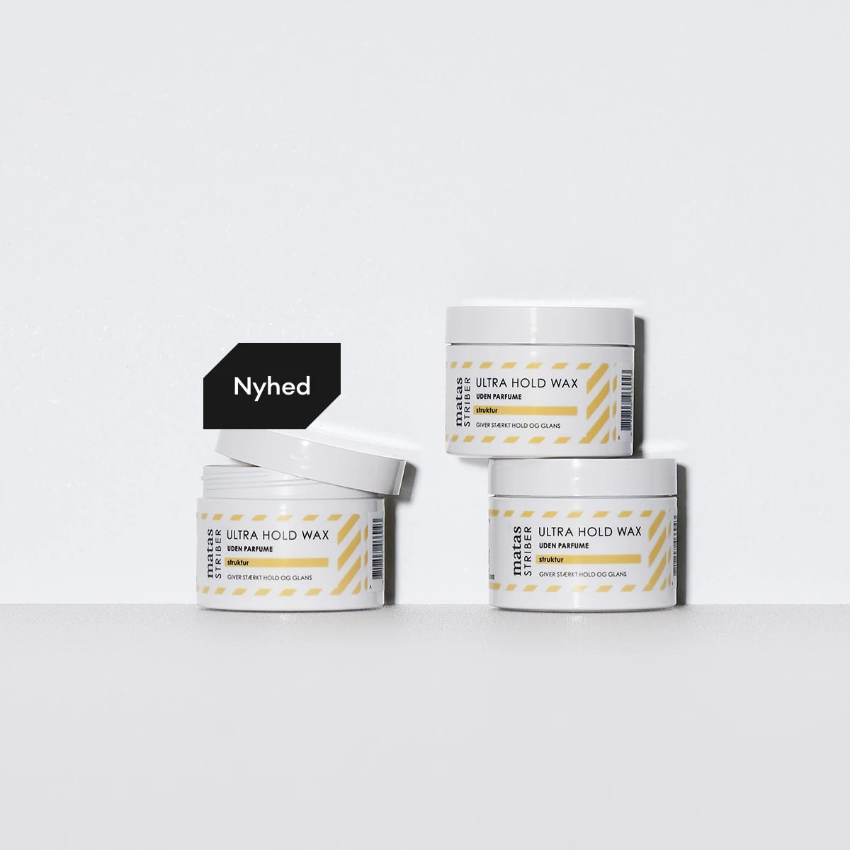 Nyhed: Tre hvide krukker med Matas Striber Ultra Hold Wax, uden parfume, der giver stærkt hold og glans. En krukke har åbent låg.