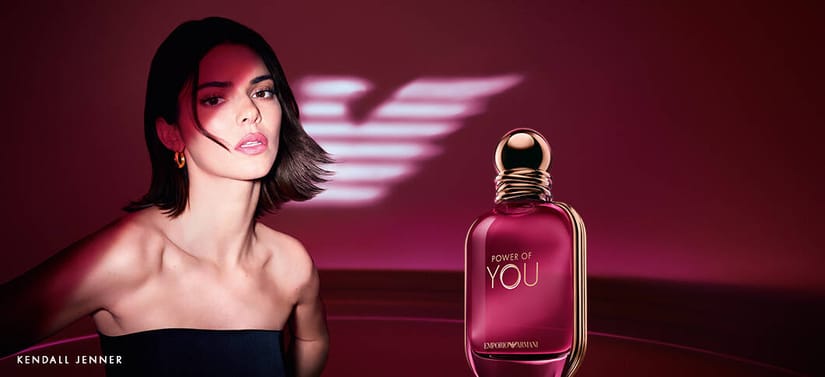 Her ses et billede med en Kendal Jenner placeret til venstre mod en rød baggrund samt en parfumeflakon til højre. På flakonen står teksten “POWER OF YOU” og “EMPORIO ARMANI”. Nederst til venstre i billedet står teksten “KENDALL JENNER”.