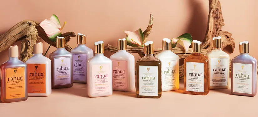 Her ses en masse forskellige Rahua produkter op en række. Baggrunden har en sart lyserød farve og der er desuden er gammel gren liggende bagved produkterne. 