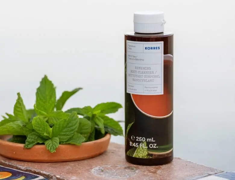 Her ses en hvid baggrund med et brunt Korres produkt på et bord, hvor der også er en plante. 