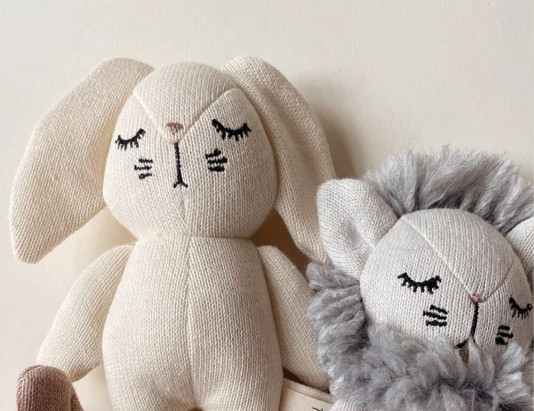 To dekorative produkter til børn: en grå strikket løvebamse og en cremefarvet tandformet taske med ansigt og brune hanke.