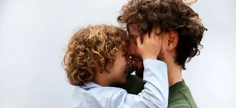 Her ses en far, som holder sin søn. De har ansigterne mod hinanden og sønnen holder på farens kinder.